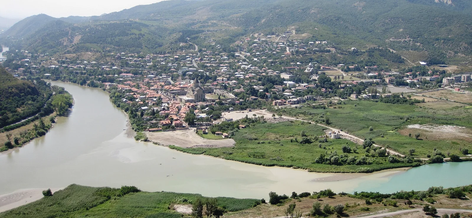 The Aragvi and the Mtkvari meeting below Mtskheta, seen from the Jvari ridge. The pale water of one river and the turquoise of the other run on together without mixing.