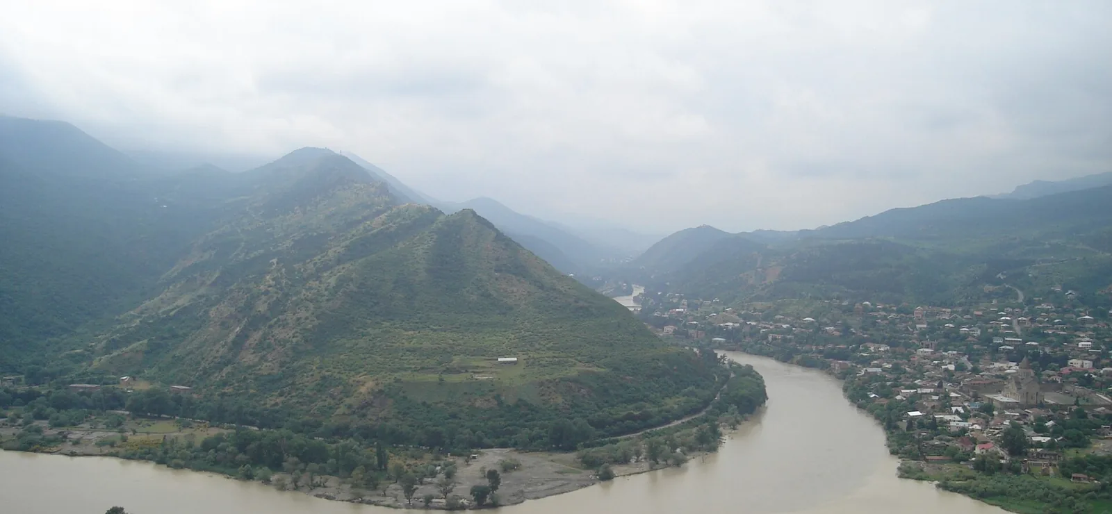 The Aragvi and the Mtkvari meeting below Mtskheta, under low cloud, the wide brown bend of the river running past the town.