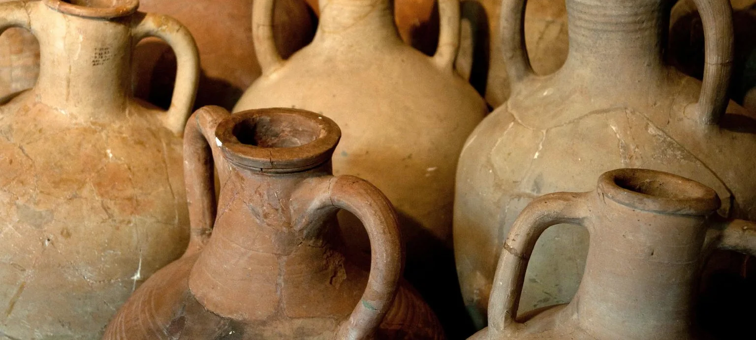 Ancient two handled clay amphorae packed shoulder to shoulder in warm low light